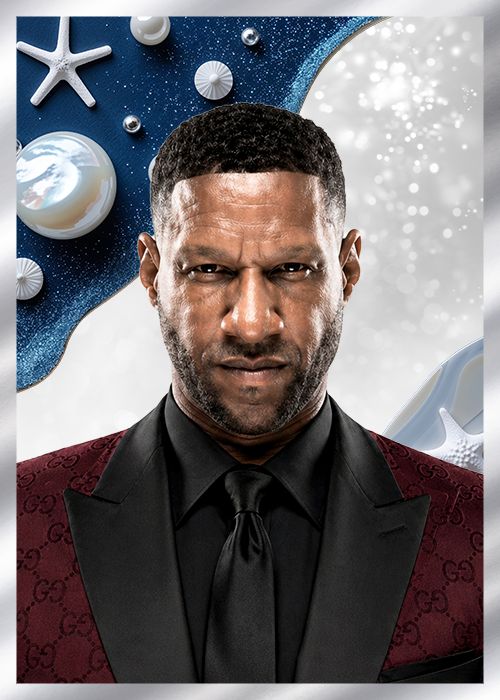 A close-up portrait of a serious-looking Black man wearing a burgundy suit and black tie against a starry blue background with seashells.
