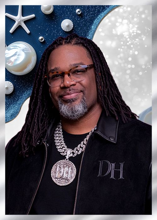 A man with dreadlocks wearing a black jacket with "DH" printed on it, standing in front of a starry blue background with seashells.