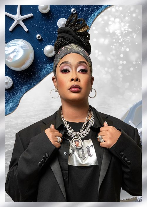 A person wearing a black jacket, large jewelry, and an elaborate headpiece with stars against a blue and white background with seashells.