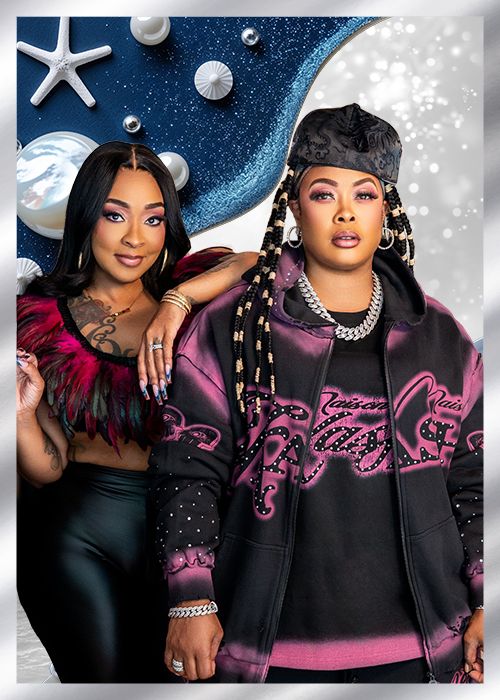 Two women wearing colorful, embellished outfits posing in front of a space-themed backdrop with stars and planets.