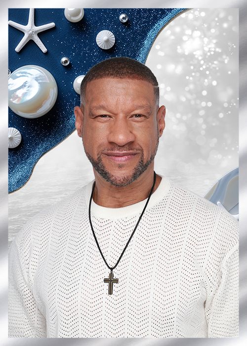 A man with a beard wearing a white sweater and a cross necklace, against a backdrop of starry blue and white sparkles.