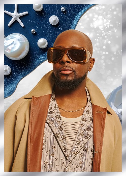 A man wearing sunglasses and a beige coat stands in front of a blue background with starfish and seashells.